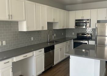 Farmhouse sinks, white cabinets, and grey quartz counter tops in select units